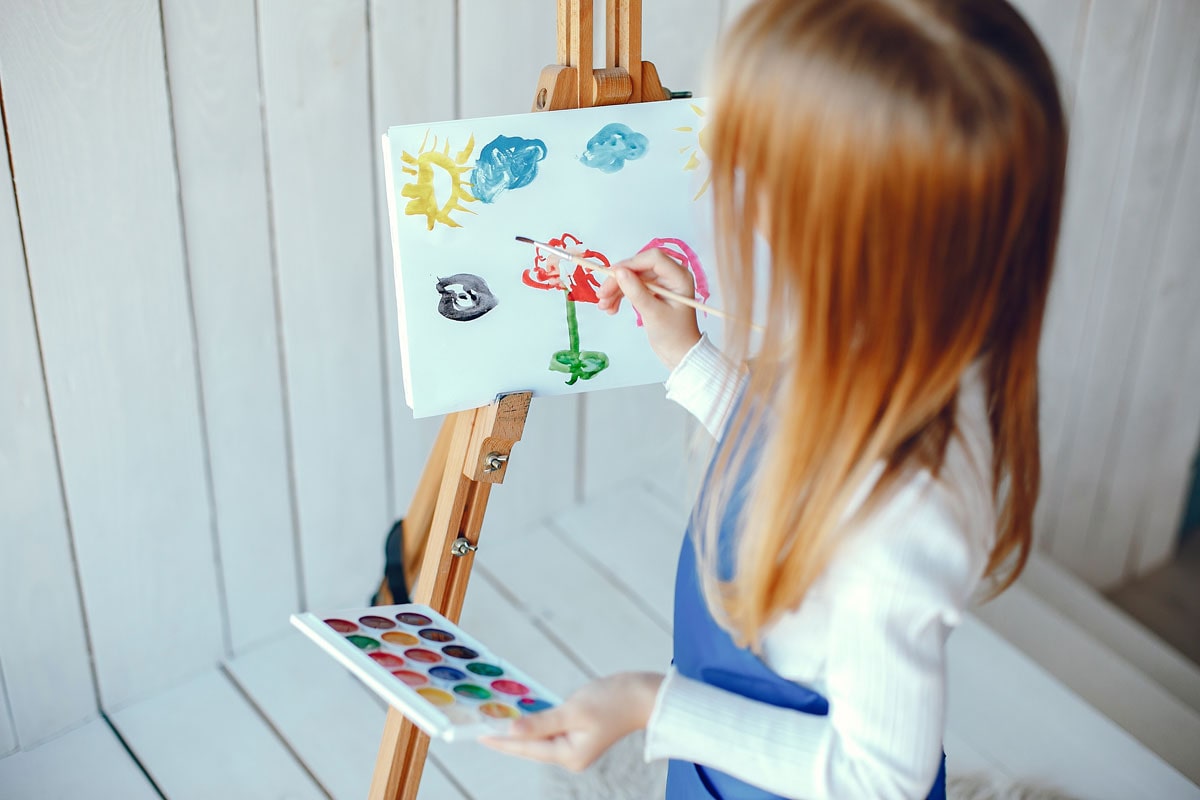 Cute little girl in a blue apron. Child painting at home
