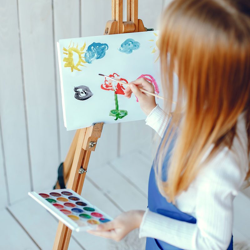 Cute little girl in a blue apron. Child painting at home